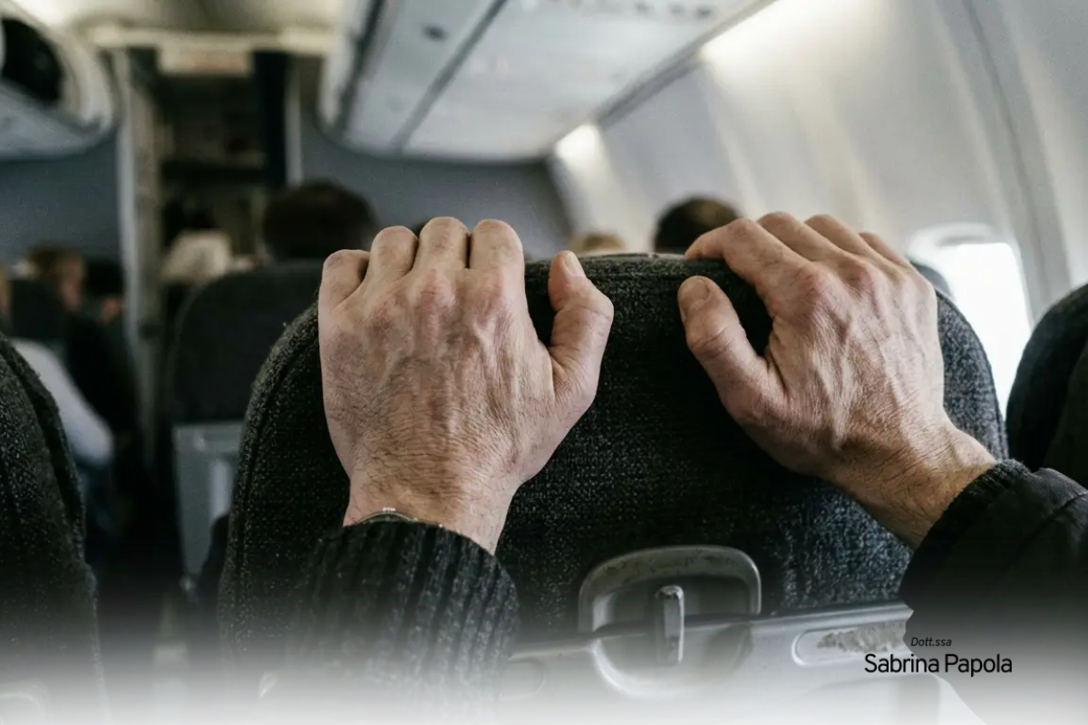 Mani strette sui braccioli del sedile durante un volo, segno di ansia e tensione | Sabrina Papola